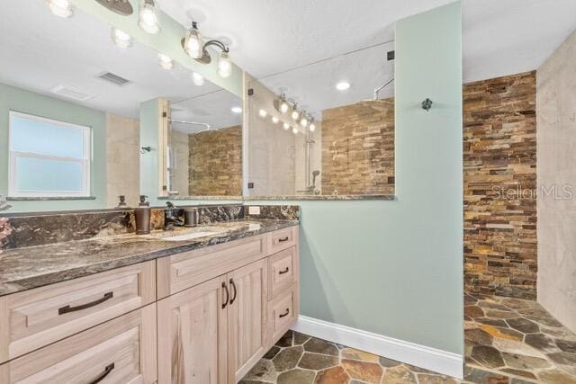 bathroom with visible vents, stone finish floor, vanity, tiled shower, and baseboards