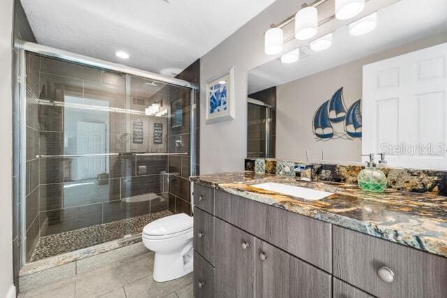 bathroom featuring toilet, a shower stall, tile patterned flooring, and vanity