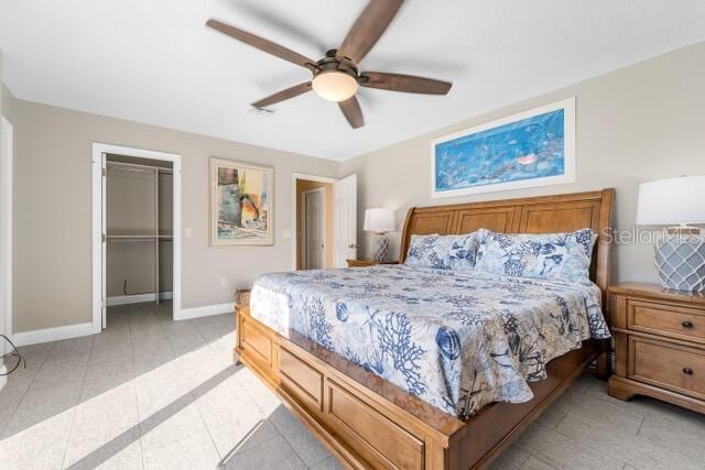 bedroom featuring baseboards, a ceiling fan, a walk in closet, a closet, and light tile patterned flooring