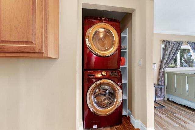 clothes washing area featuring stacked washer / dryer, laundry area, baseboards, and wood finished floors