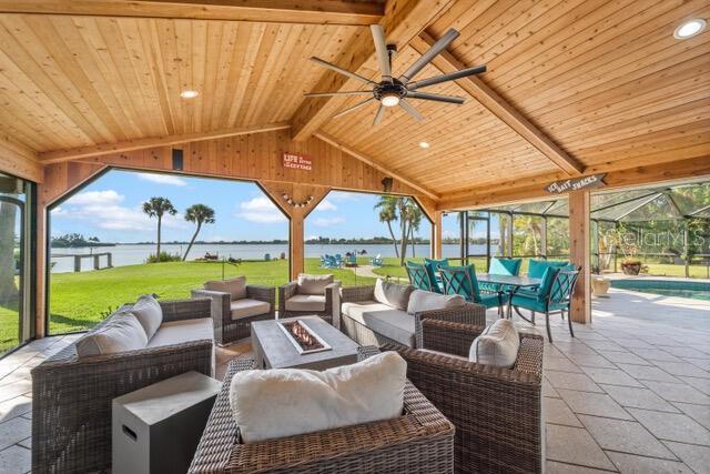 view of patio / terrace with ceiling fan, glass enclosure, a water view, and an outdoor living space with a fire pit