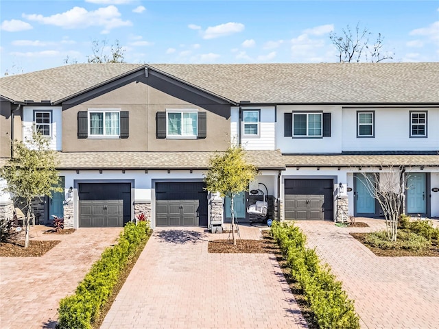 multi unit property with stone siding, an attached garage, driveway, and stucco siding