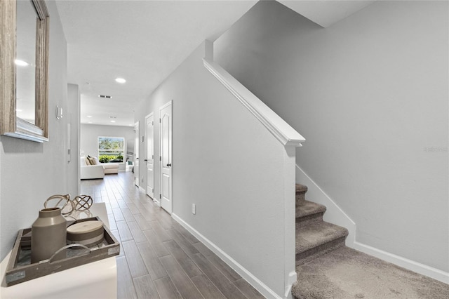 corridor featuring dark wood-type flooring, stairway, visible vents, and baseboards