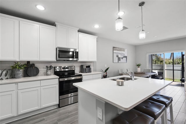 kitchen with light countertops, decorative backsplash, appliances with stainless steel finishes, a sink, and an island with sink