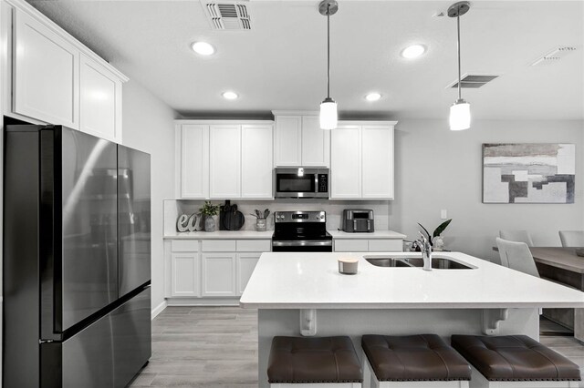 kitchen featuring decorative light fixtures, visible vents, appliances with stainless steel finishes, light wood-style floors, and a sink