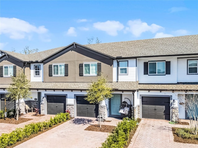 townhome / multi-family property with a shingled roof, stone siding, driveway, and an attached garage