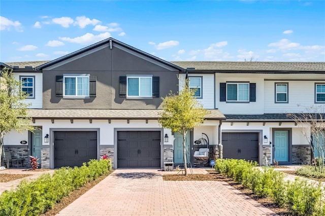 townhome / multi-family property featuring a garage, stone siding, driveway, and stucco siding