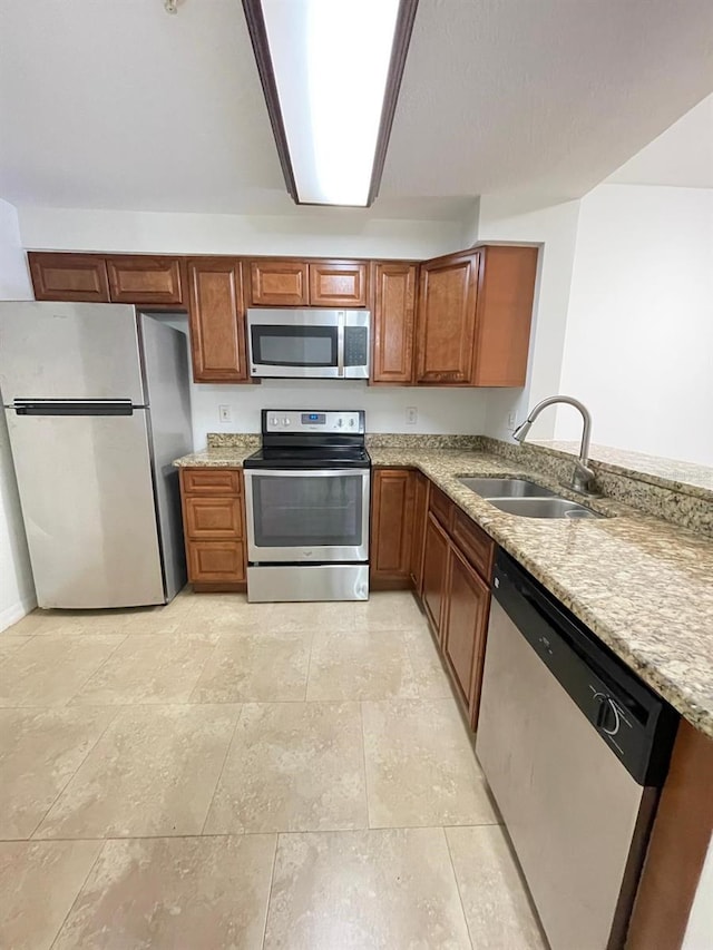 kitchen featuring light stone countertops, appliances with stainless steel finishes, a peninsula, brown cabinetry, and a sink