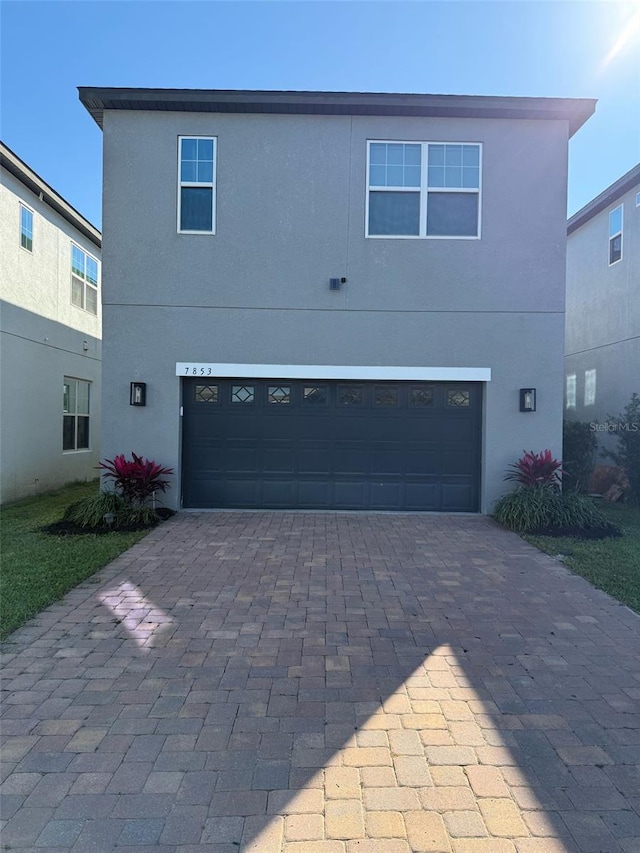 view of front of property featuring decorative driveway, an attached garage, and stucco siding