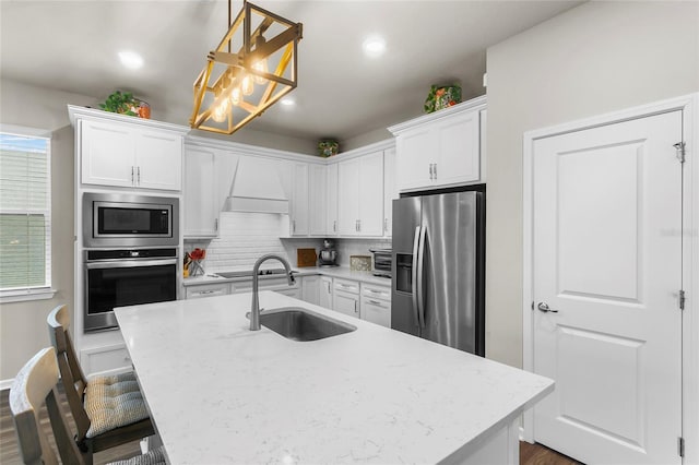 kitchen with white cabinets, appliances with stainless steel finishes, a sink, premium range hood, and backsplash