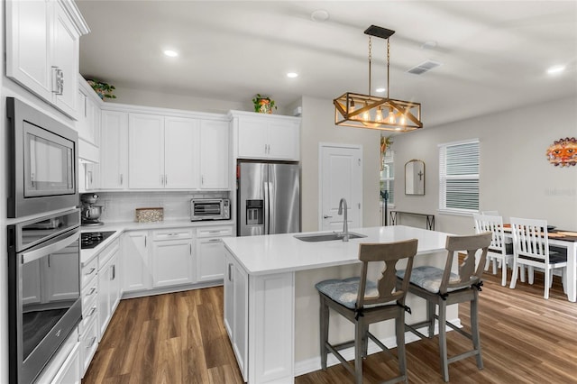 kitchen with a toaster, stainless steel appliances, a sink, backsplash, and dark wood-style floors