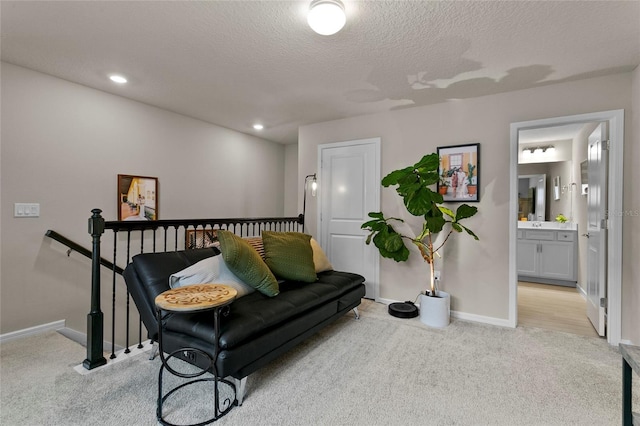 living area featuring light carpet, baseboards, a textured ceiling, and an upstairs landing