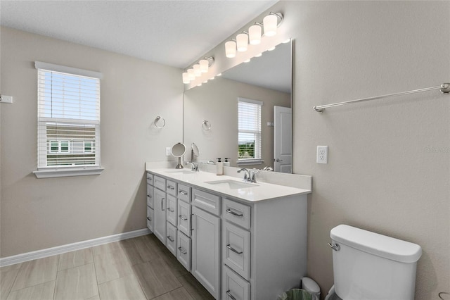 bathroom with double vanity, a sink, toilet, and baseboards