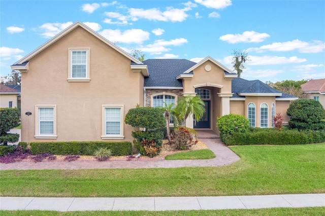 view of front facade featuring a shingled roof, a front yard, and stucco siding