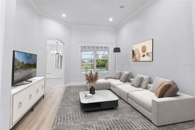 living area featuring arched walkways, light wood-style flooring, recessed lighting, baseboards, and crown molding