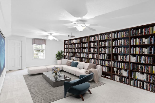 living area featuring a ceiling fan, bookshelves, and carpet flooring