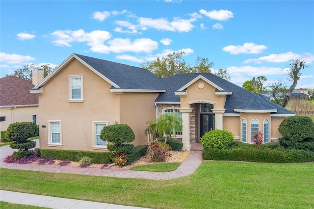 view of front facade featuring roof with shingles, a chimney, a front lawn, and stucco siding