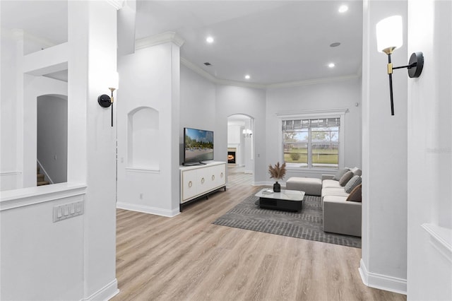 living room featuring baseboards, crown molding, arched walkways, and wood finished floors