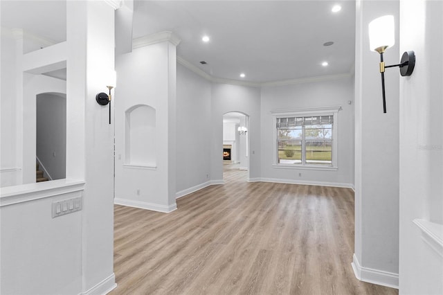 interior space with crown molding, recessed lighting, light wood-style flooring, a lit fireplace, and baseboards