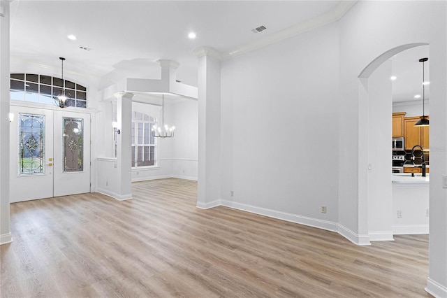 foyer entrance with a chandelier, arched walkways, ornamental molding, light wood finished floors, and ornate columns