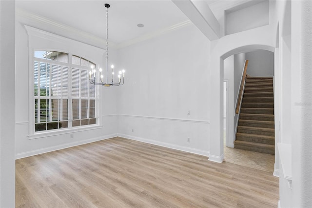 unfurnished dining area featuring arched walkways, crown molding, stairway, light wood-style flooring, and baseboards