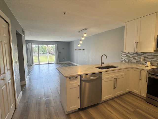 kitchen with dark wood finished floors, appliances with stainless steel finishes, open floor plan, a sink, and a peninsula