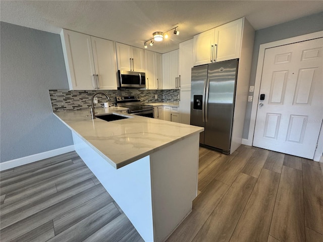 kitchen featuring a peninsula, a sink, white cabinets, appliances with stainless steel finishes, and decorative backsplash