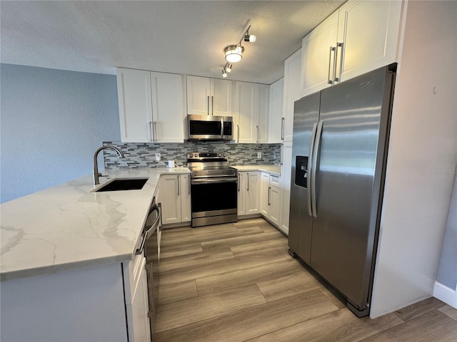 kitchen featuring light stone counters, a sink, stainless steel appliances, light wood-style floors, and backsplash