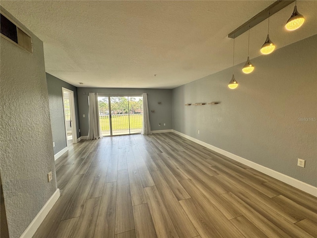 empty room with visible vents, a textured wall, a textured ceiling, wood finished floors, and baseboards