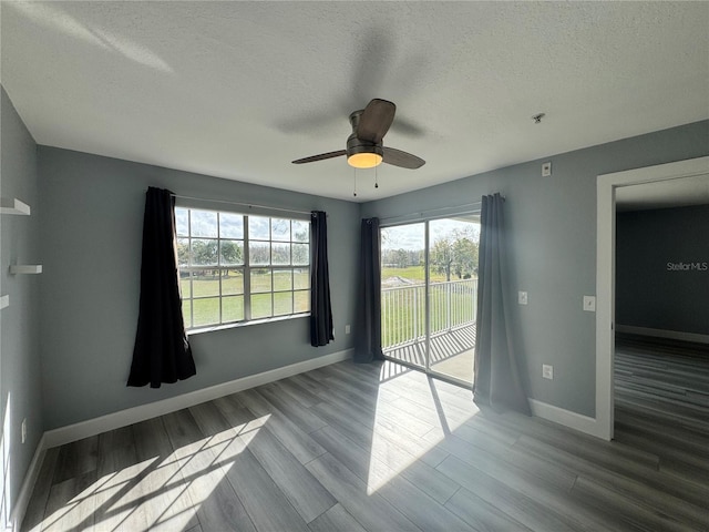 spare room featuring a textured ceiling, wood finished floors, a ceiling fan, and baseboards