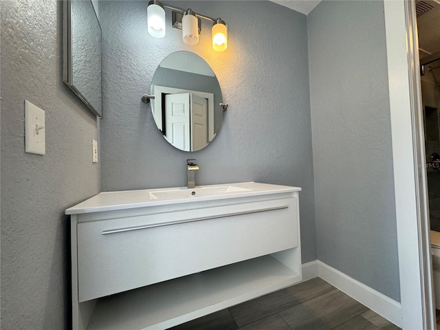 bathroom with a textured wall, baseboards, wood finished floors, and vanity