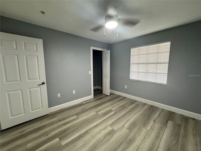 unfurnished bedroom with a ceiling fan, a textured ceiling, baseboards, and wood finished floors