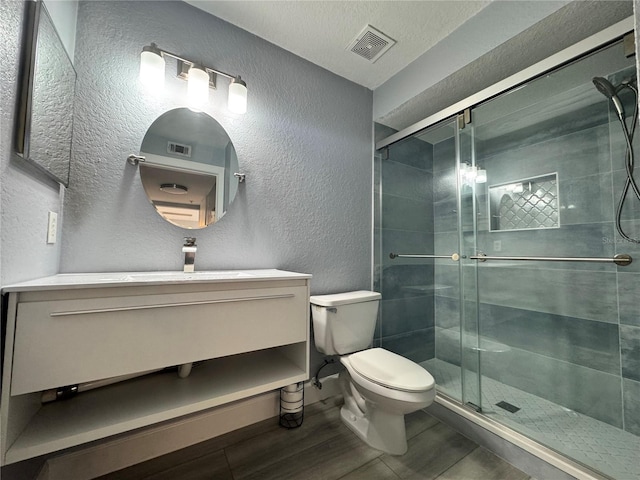 bathroom featuring a stall shower, visible vents, a textured wall, toilet, and vanity