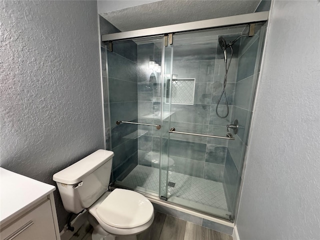 bathroom featuring a textured wall, vanity, toilet, and a shower stall