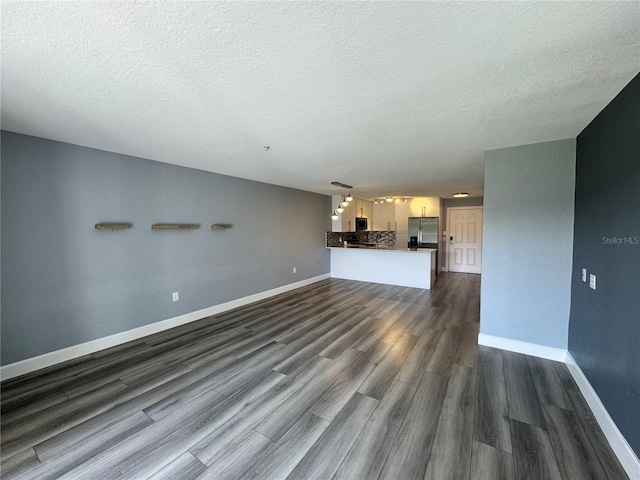 unfurnished living room with dark wood finished floors, a textured ceiling, and baseboards