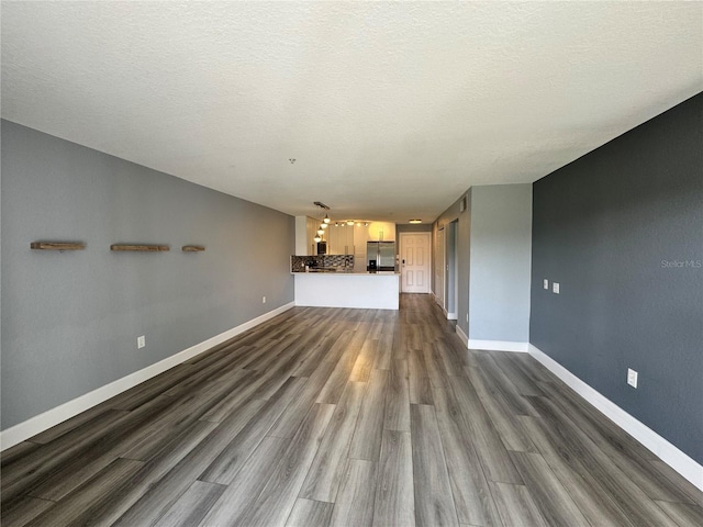 unfurnished living room with dark wood-type flooring, a textured ceiling, and baseboards