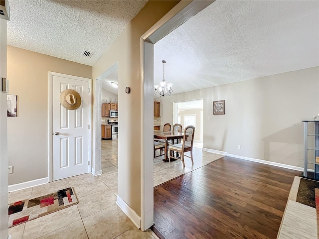 entrance foyer featuring a textured ceiling, a notable chandelier, visible vents, and light wood-style floors