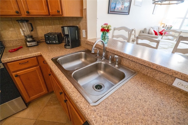 kitchen featuring a sink, tasteful backsplash, brown cabinetry, light countertops, and light tile patterned floors