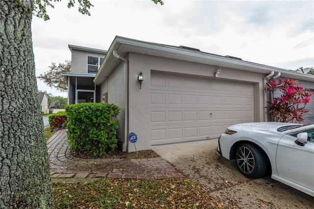 view of home's exterior featuring stucco siding, driveway, an attached garage, and a sunroom