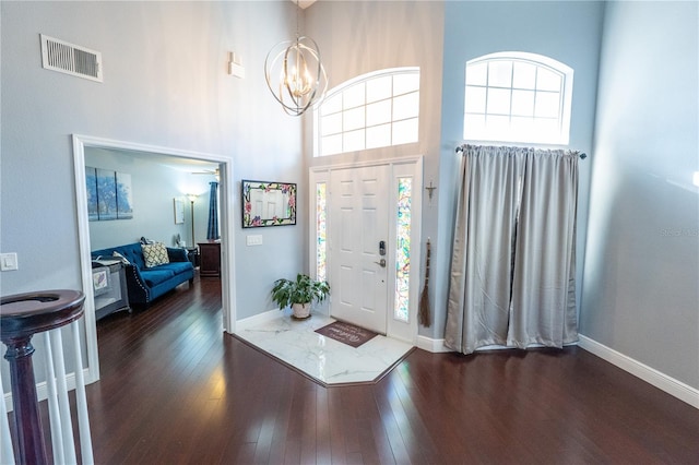 foyer entrance with baseboards, visible vents, a towering ceiling, dark wood-type flooring, and a notable chandelier