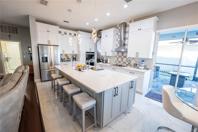 kitchen featuring marble finish floor, wall chimney exhaust hood, visible vents, and stainless steel appliances