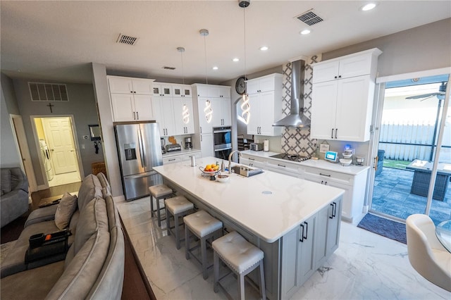 kitchen featuring marble finish floor, a sink, wall chimney range hood, stovetop, and stainless steel fridge with ice dispenser