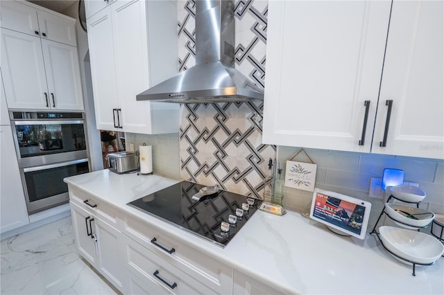 kitchen with marble finish floor, double oven, white cabinets, stovetop, and wall chimney exhaust hood