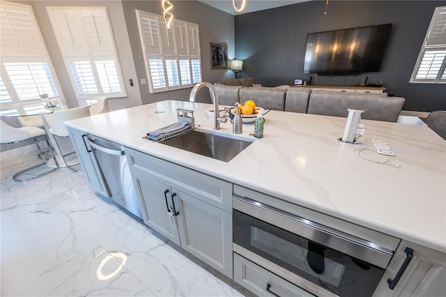 kitchen featuring light stone counters, open floor plan, a sink, marble finish floor, and stainless steel dishwasher