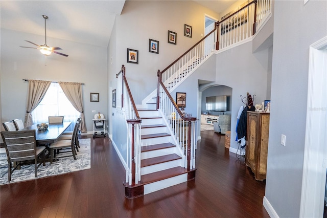 stairway featuring arched walkways, a towering ceiling, hardwood / wood-style floors, ceiling fan, and baseboards