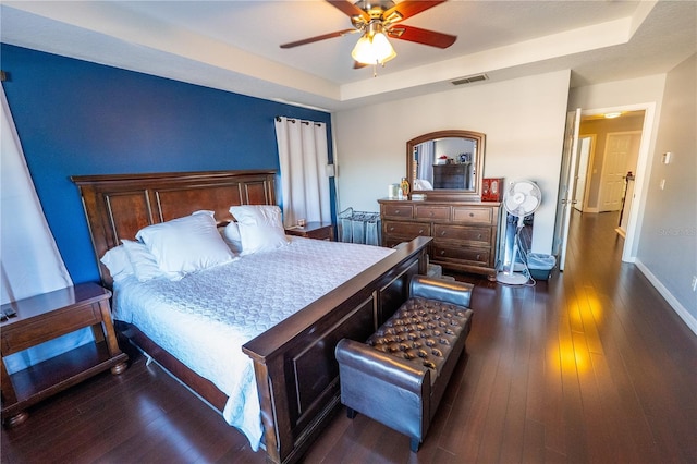 bedroom with baseboards, visible vents, a raised ceiling, and dark wood finished floors