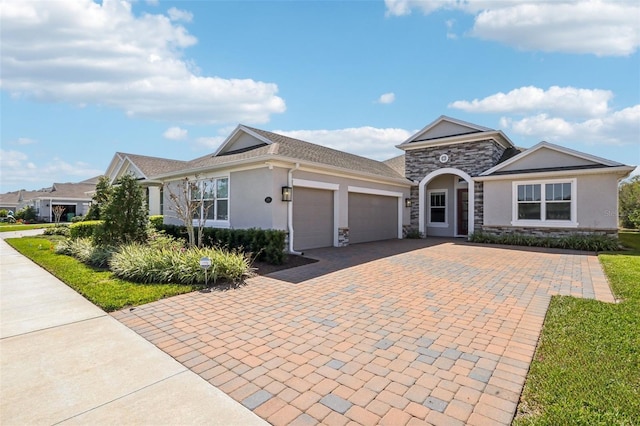 view of front of house featuring decorative driveway, stone siding, an attached garage, and stucco siding