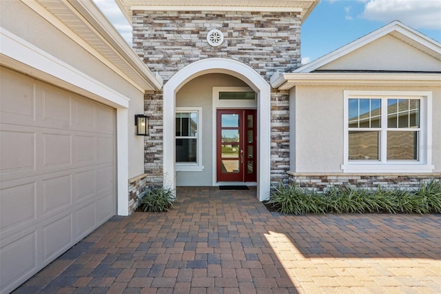 property entrance featuring an attached garage, stone siding, and stucco siding