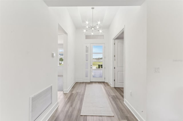 foyer entrance with visible vents, a notable chandelier, light wood-style flooring, and baseboards