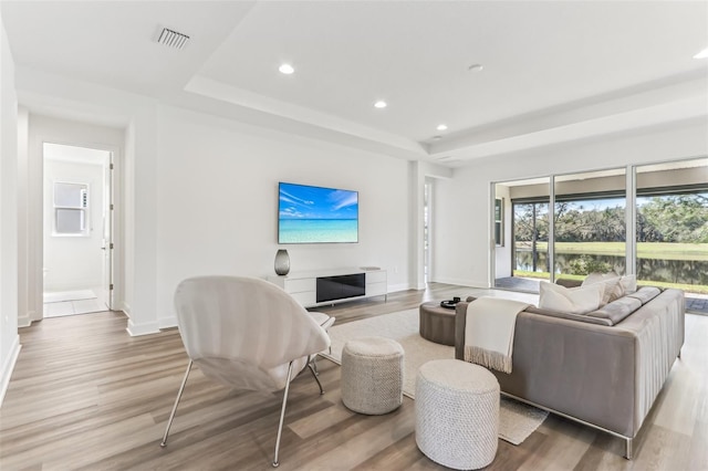 living area with light wood finished floors, a tray ceiling, and visible vents